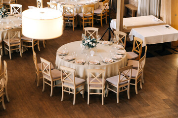 Beige wooden chairs stand at round dinner tables in the restaurantin/ Wedding day