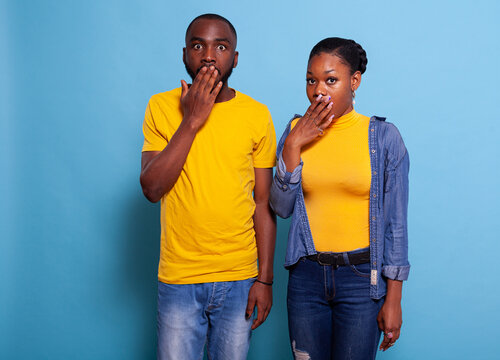 Couple having shocked facial expressions after hearing gossip. Astonished and stupefied people covering opem mouth with hand, finding out unexpected rumour. Surprised man and woman