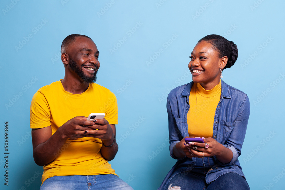 Poster man and woman holding smartphones and smiling at each other, using mobile phones with touch screen t