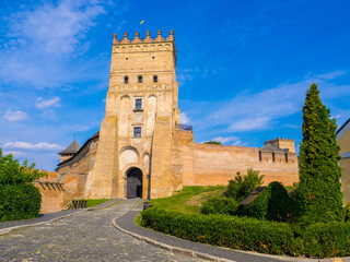 Lutsk High Castle, also known as Lubart's Castle. Ukraine. Brick Tower and Walls. A part of defence wall of Lutsk Castle. The Entrance tower against the blue sky and with greenery under a brick wall.