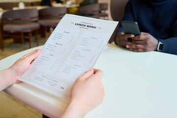 Close-up of unrecognizable woman reading menu while sitting at table with her colleague during business lunch in cafe