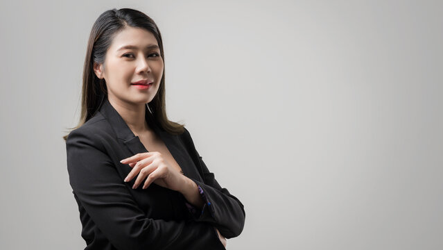 Smiling asian business woman pointing up and looking at the camera over gray background