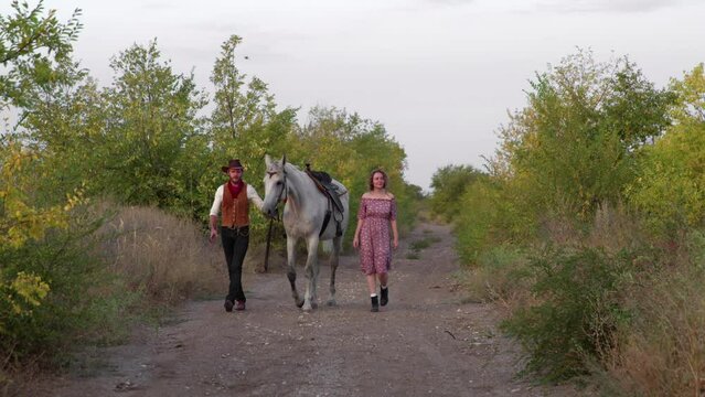 Lovely couple handsome cowboy, beautiful woman and horse walks together