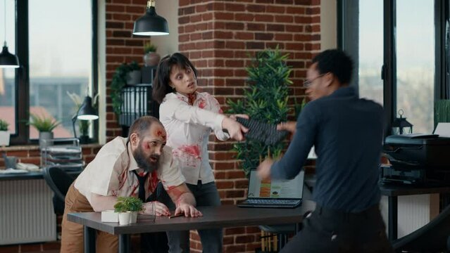 Frightened businessman attacked by dangerous zombies in office. Terrified worker defending himself from dangerous brain-eating monster with deep and bloody wounds in company workspace.