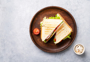 Club sandwich on a wooden plate of ham cheese, cucumber, tomato and lettuce leaves on a blue...