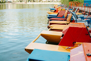 Fototapeta na wymiar Boat station of catamarans in park on sunny day. Side view of parked multicolored catamarans on water. Selective focus, copy space