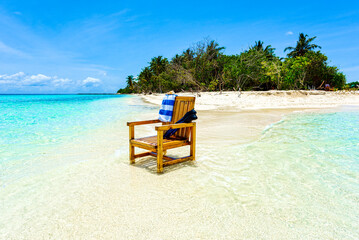 A wooden chair standing in the Indian Ocean with a towel, shell and flippers.