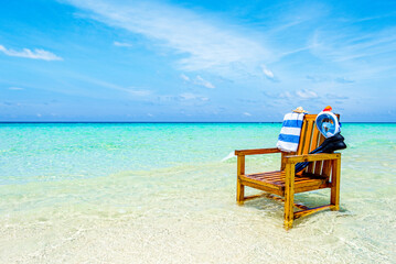 A wooden chair in the Indian Ocean with a towel, shell, flippers and inderwater mask.