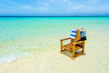 A wooden chair in the Indian Ocean with a towel, shell, flippers and inderwater mask.