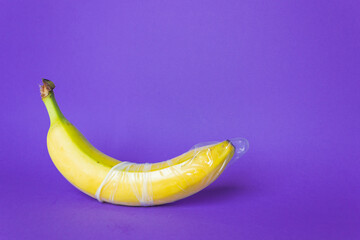 Banana fruit with latex transparent condom isolated on a purple background. Safe sex concept.