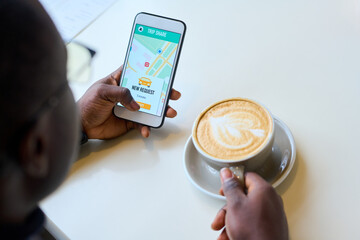 Close-up of businessman ordering taxi through an app on his smartphone while drinking cappuccino at table