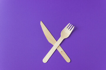 Disposable tableware from natural materials - wooden fork and knife lie on a violet background crosswise.