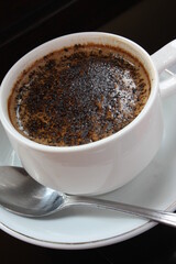 A cup of hot chocolate espresso coffee. With chocolate sprinkles. White cup and saucer. One stainless spoon. Black background. Close up top view.