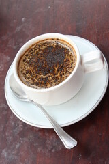 A cup of hot chocolate espresso coffee. With chocolate sprinkles. White cup and saucer. One stainless spoon. Black background. Close up top view.