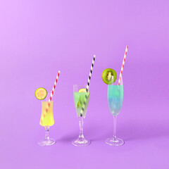 Three spring cocktails on purple background with copy space. Party or refreshment beverage with garnish and straws. Minimal holiday concept.