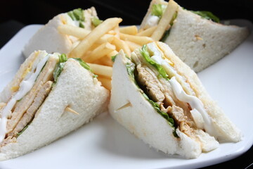 Triangular shaped sandwich. Stuffed thick meat, thin cheese, mayonnaise, lettuce. Pierced with a toothpick. On a white ceramic plate. close up.