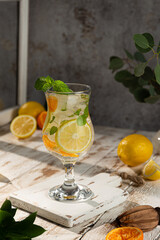 Ice-cold non-alcoholic lemon cocktail decorated with a sprig of mint on a light wooden background. Close-up