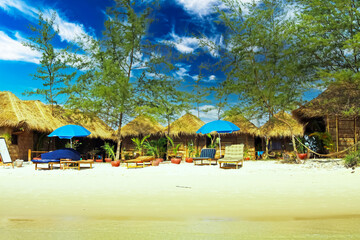 Sihanoukville area, Cambodia - December 9. 2009: Beautiful idyllic white sand beach, simple basic bamboo hut resort, green trees, umbrellas, loungers (focus on central huts)