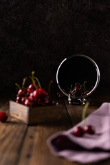 Cherry with water drops in a wooden box on a wooden table. Focus on the cherry that is reflected in the mirror