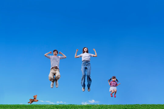 青空を背景に親子三人で元気よくジャンプしている様子。仲良し,元気,健康のイメージ