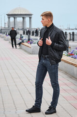 A young handsome guy in a black jacket on a river embankment with a large rotunda in the...