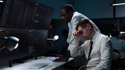 Stressed diverse stock market traders looking at multi-screen computer station with graphs. Brokers...
