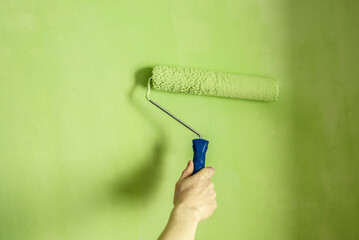 Hand is painting the wall green with a roller. Concept of renovation in the apartment. Closeup and copy space