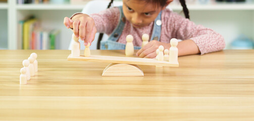Unidentified little girl is trying how to balance the wooden people model on the scale, concept of learn through play, montessori, homeschool, creativity, stem education and child development.