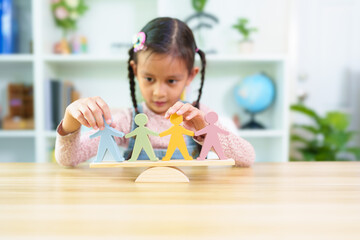 Blurred of cute asian little girl is trying to balance the people model on the wooden scale, concept of homeschool, montessori, learning, education and conceptual of equality, diversity, fairness.
