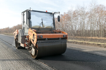 New road with asphalt pavement texture on a damaged highway. Asphalt road roller with heavy...