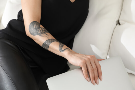 Beautiful woman with tattoos on arm using laptop indoors, closeup