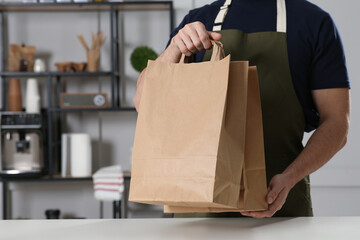 Worker with paper bags at counter in cafe, closeup. Space for text