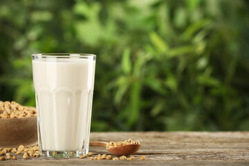 Glass with fresh soy milk and grains on white wooden table against blurred background. Space for...