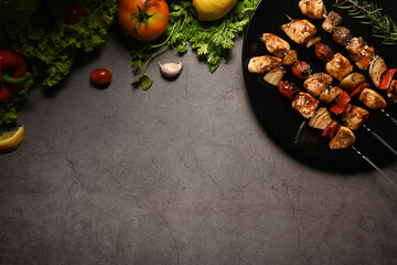 Plate with grilled chicken meat skewers and fresh vegetables on dark stone background. Copy space for your text