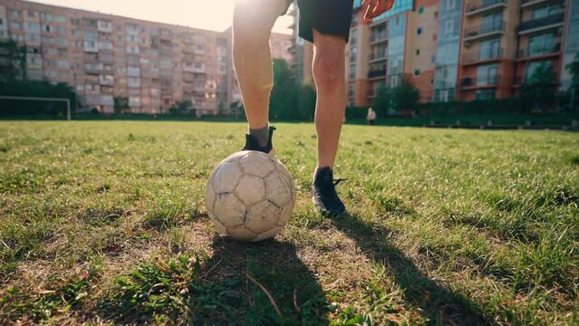 A teenage boy in a sports uniform hits the ball on the football field. The guy runs and kicks the ball. Skills training at a stadium with a natural surface in the city. Green grass. Sunshine