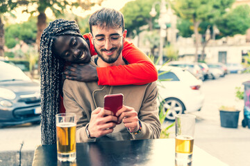 Smiling young multiracial couple embracing while looking at smartphone - Multiethnic couple sharing...