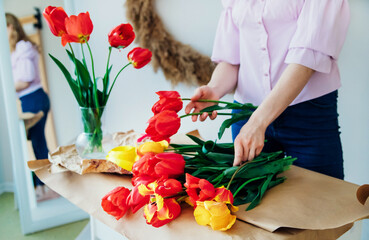 Women's hands pack a festive bouquet in wrapping paper. The florist makes an assembly with red...