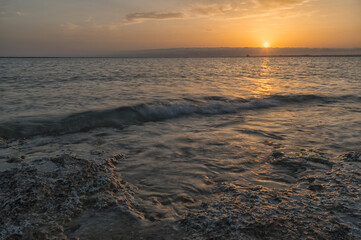 Fototapeta premium Tramonto sul mare con cielo nuvoloso e riflessi del sole sull'acqua.