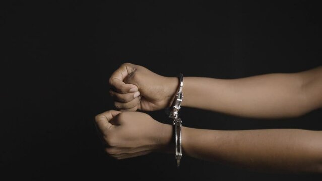 Close up shot of hands removing cuffs from hand on black dark background - concept of freedom, releasing and liberty.