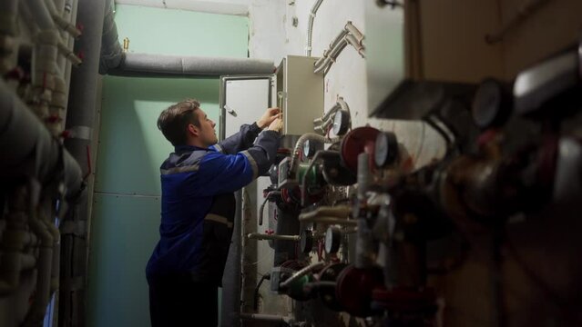 Electrician disassembles electrical fuse box. Master in uniform screwing electrical panel to fix electricity. Man checking control panel in technical room of in a district heating substation.