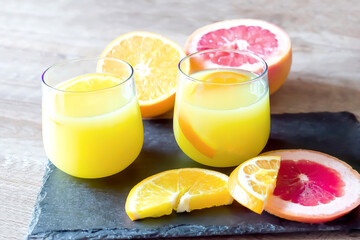 close up oranges and grapefruits coctails in glasses, fresh juice with fruits on cutting black...