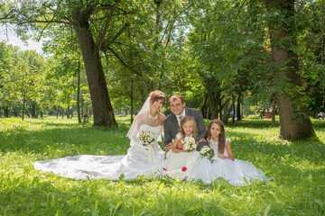 The groom in a suit and the bride in a long white dress with children in summer dresses in a spring...