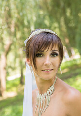 Bride in a white dress among the greenery in the summer garden.