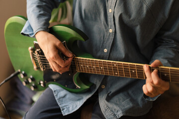 Close-up of a musician playing a green electric guitar and wearing denim clothes. Blurred...