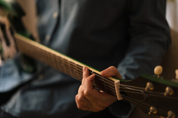 Close-up of a guitarist hand, playing a green electric guitar and wearing denim clothes. Blurred background.