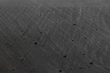 Wet black volcanic sand on shore with corner divorces, texture, background.