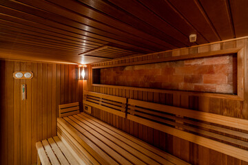 Seat in sauna room. Empty wooden steam room with stone heater. Sauna room for good health. Sauna room with traditional sauna accessories.Healthy and spa life style.
