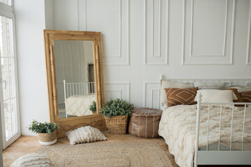 Bright and spacious bedroom with a white wall, an eco-wooden mirror and flower pots. Cozy bright...