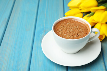 Cup of aromatic coffee and beautiful yellow tulips on light blue wooden table, space for text. Good morning