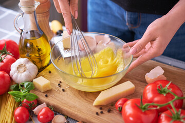 Woman beating egg yolks with a whisk making homemade pasta carbonara